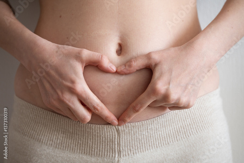 Woman forming a heart shape with her hands on her belly, celebrating body positivity and embracing fertility and motherhood