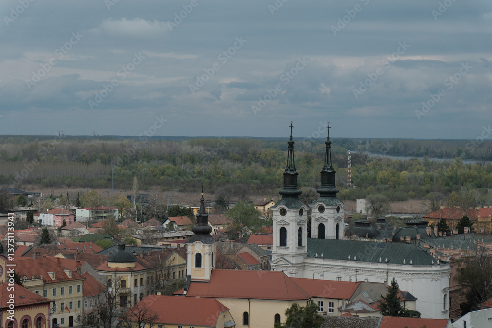 Obraz premium Panoramic view of Sremski Karlovci, Serbia, featuring Saint Nicholas Cathedral, historic baroque buildings, and the Danube River. Captured in spring under dramatic cloudy skies.