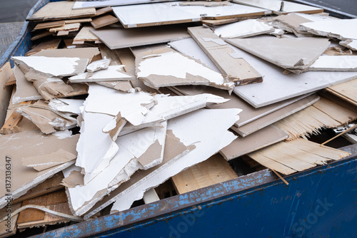  heap of shattered drywall and gypsum decorations is removed as construction waste. Broken building tiles and debris are collected in a container during renovation