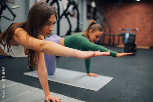 Two young women doing bird dog exercise in gym