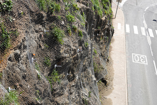 Obraz na płótnie Workers implement netting and other methods to stabilize a rocky hillside along a roadside. w salonie