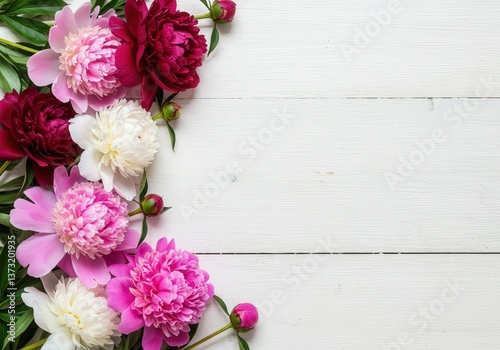 Overhead view of colorful peonies in full bloom arranged on a clean, white wooden background.
