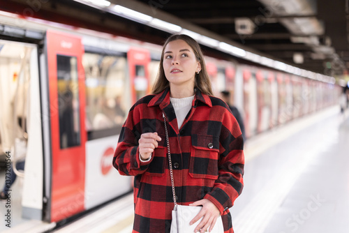 During long wait for transport, passenger girl standing and spends time on platform of metro station, waits for arrival of train, prepares to meet friend at public transport stop