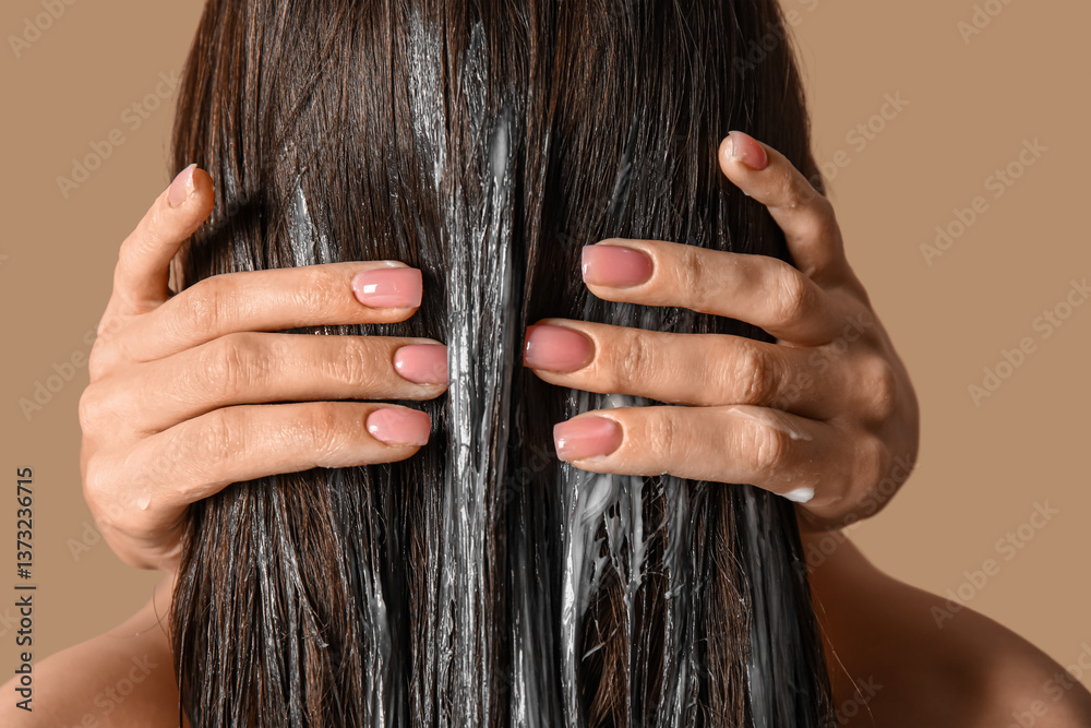 Obraz premium Young woman using cosmetics for hair treatment on beige background, closeup