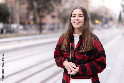 During long wait for transport, passenger girl standing and spends time on platform of tram station, waits for arrival of transport, prepares to meet friend at public transport stop