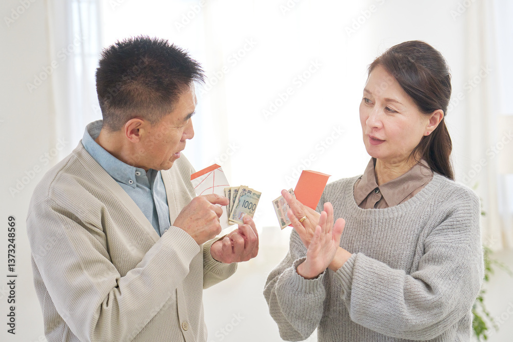 ポチ袋を持ってお年玉の金額を相談するシニア男性と女性 ポチ袋を持ってお年玉の金額を相談するシニア男性と女性