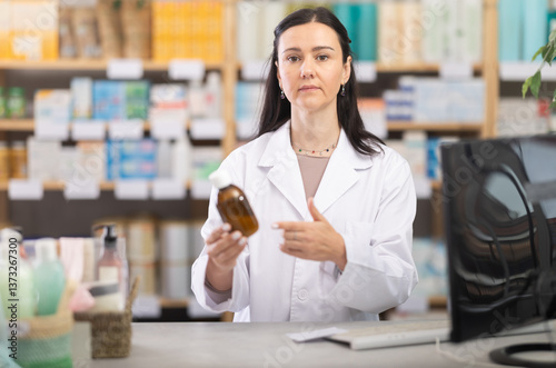 Focused middle-aged female apothecary taking records of stock using tablet in chemistry