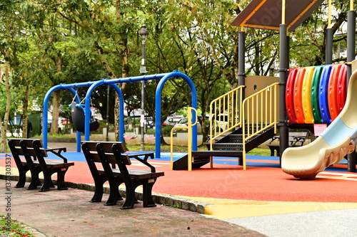 Obraz na płótnie The photo captures an outdoor playground in a park, featuring a slide and swings for children’s recreational activities. Adjacent benches provide a convenient resting spot for families. w salonie
