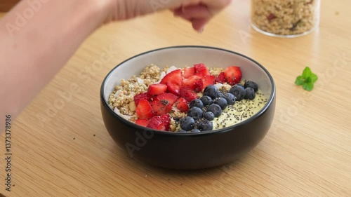 Preparation of a delicious granola bowl with fresh berries and chia seeds on a wooden table