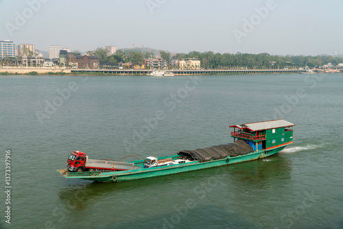 CHIANG SAENN, THAILAND - APRIL 30, 2024: A boat loaded with cars sails along the Mekong River between Thailand and Laos.