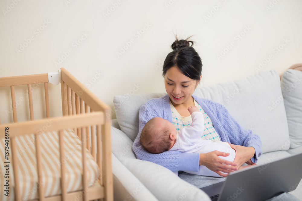 Mother holding baby while working on laptop at home