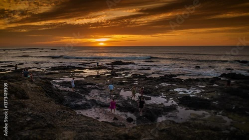 rocky coastline time lapse with setting sun and open ocean and long exposure people moving around the coast