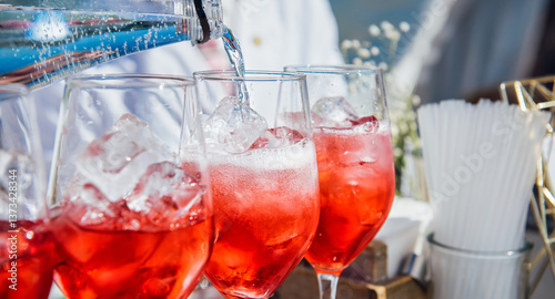 The bartender pours soda into a glass of wine with ice in close-up. Creating a red cocktail, wine, juice, liqueur, bubbling water. Refreshing cocktail in summertime. Beach bar, sun, cold drinks