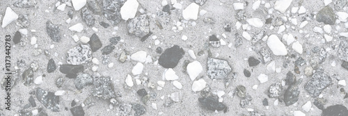 Concrete wall texture with pebbles. Decorative rough concrete surface with white, black and gray stones. Wide panoramic texture for background and design.