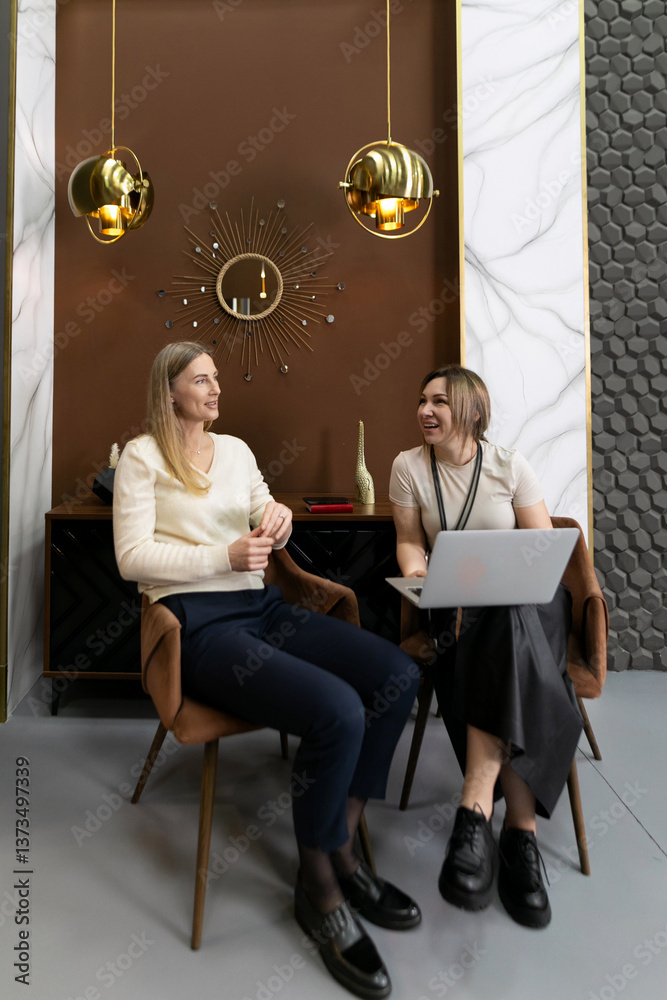 Two friends engage in a lively discussion while working on a laptop in a stylish modern interior setting