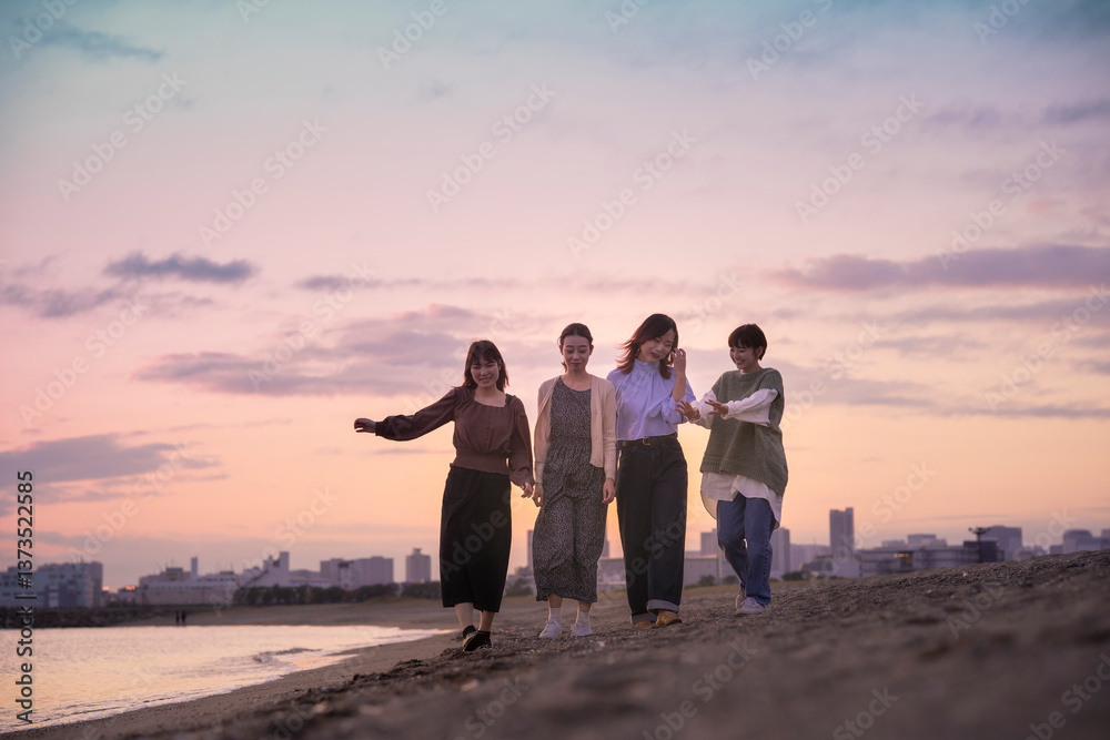 Fototapeta premium 夕暮れの中、寄り添って海沿いを歩く女性4人