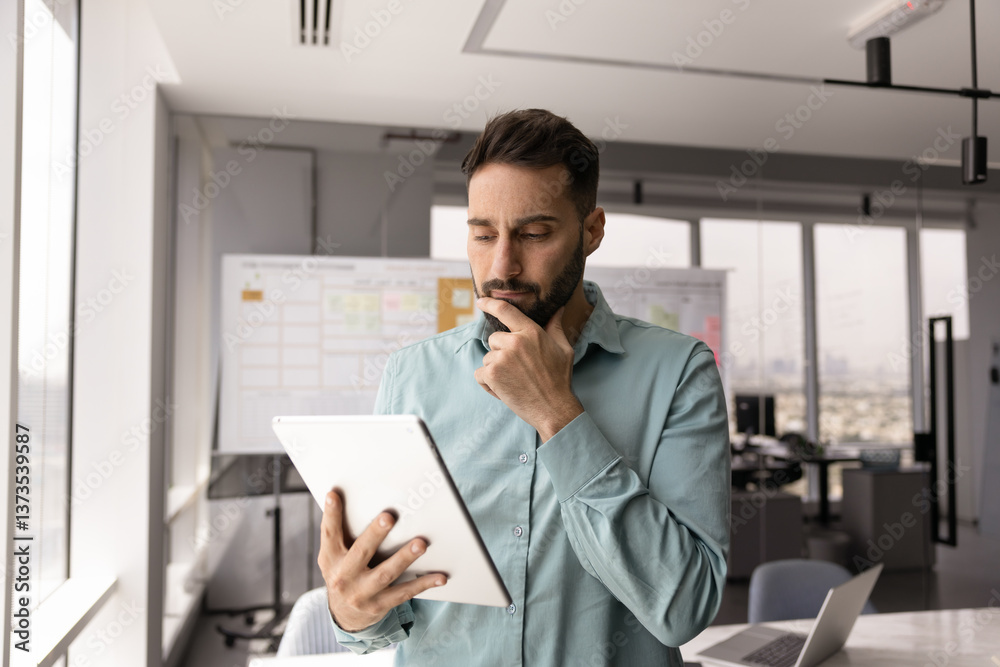 Fototapeta premium Serious thoughtful Hispanic business leader man using tablet in office workspace alone, looking ad gadget, touching chin, frowning, thinking on work challenge, problem, making decision
