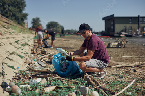 Obraz na płótnie Environmental activist cleaning river shore from piled up trash. w salonie