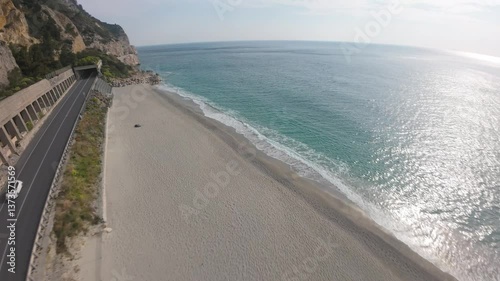 downward FPV aerial dive and skim across the majestic turquoise waters of Spiaggia del Malpasso beaches glistening in the sun photo