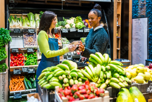 Saleswoman serving customer in organic supermarket with fresh produce