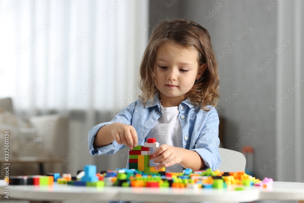 Cute girl playing with building blocks at white table indoors Cute girl playing with building blocks at white table indoors
