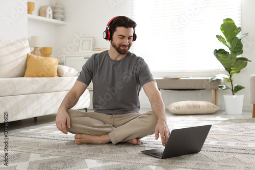 Obraz na płótnie Smiling man in headphones meditating near laptop on floor at home w salonie