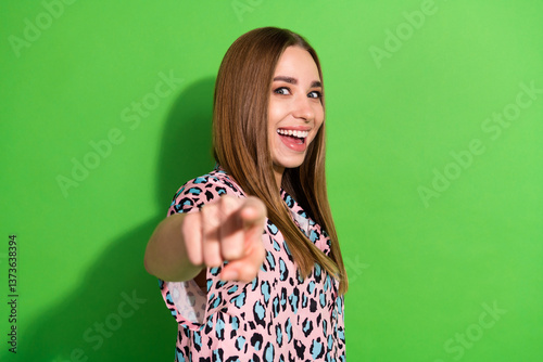 Smiling young woman in casual fashion pointing at viewer against a vibrant green background