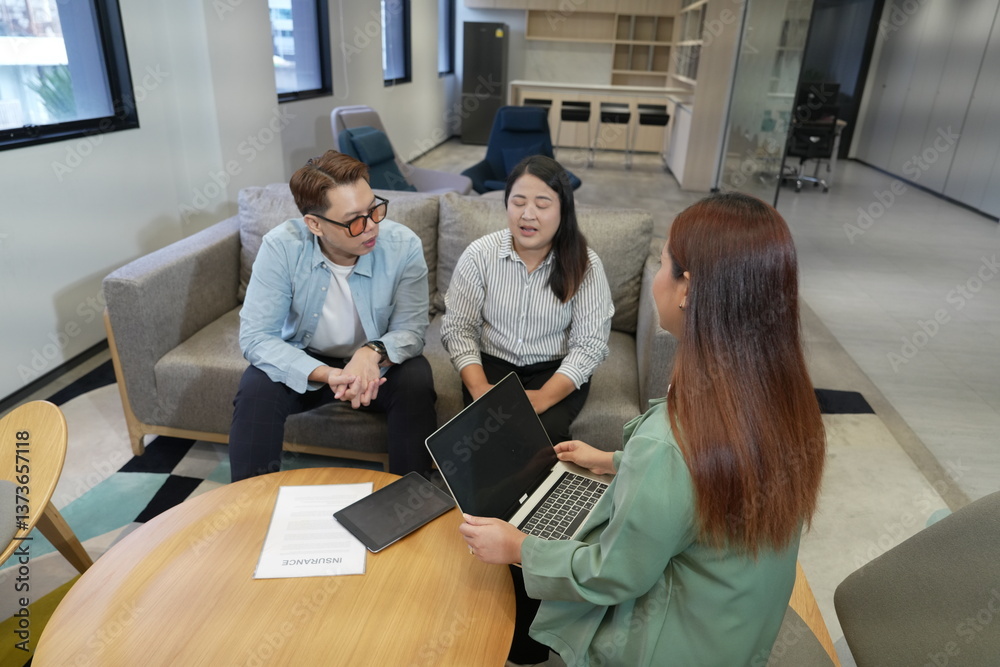 Asian female sales and marketing staff holding laptop explaining insurance presenting life insurance to male and female customers sitting in office company lounge.