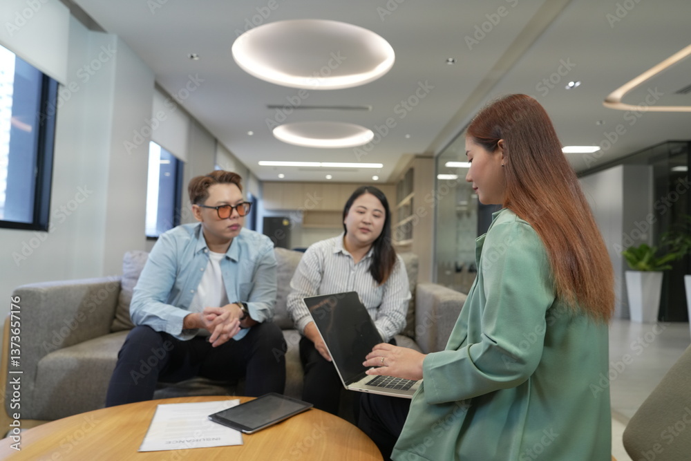 Asian female sales and marketing staff holding laptop explaining insurance presenting life insurance to male and female customers sitting in office company lounge.