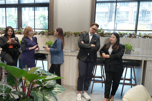 A team of Asian male and female employees in business suits take a break and chat with each other in the company lobby.