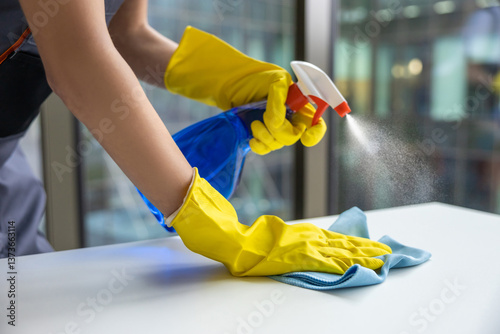 Young woman in yellow gloves cleaning the table in the office