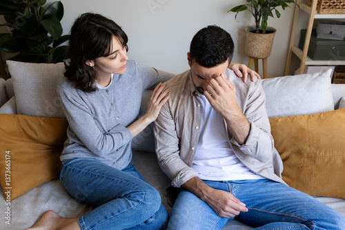 High angle view of wife consoling depressed husband sitting on the couch at home living room.