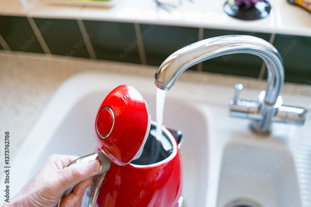 Homeowner seen filling a stylish water kettle at a kitchen sink. About to make a hot beverage while working from home.