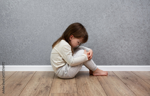 Sad and lonely child sitting alone near the wall. Domestic violence against children. photo