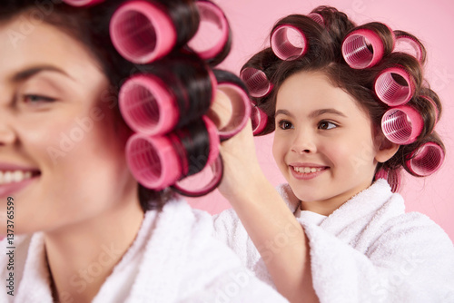 Little girl with curlers makes hairstyle to mom