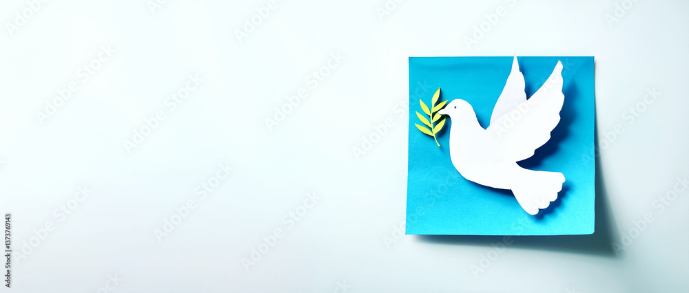 Obraz premium A white paper dove cutout holding a green olive branch on a blue square background. The minimalist design evokes themes of peace, hope, and reconciliation, ideal for symbolic or cultural projects.