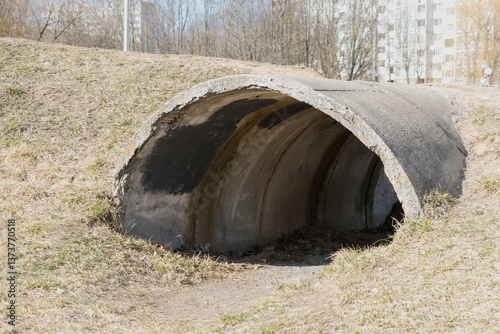 A gray concrete pipe emerging from the ground with grass nearby