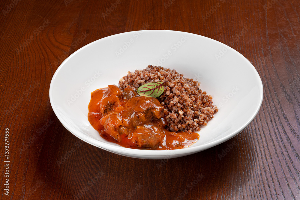 Buckwheat groats with meat in tomato sauce on a white plate on a wooden table Buckwheat groats with meat in tomato sauce on a white plate on a wooden table