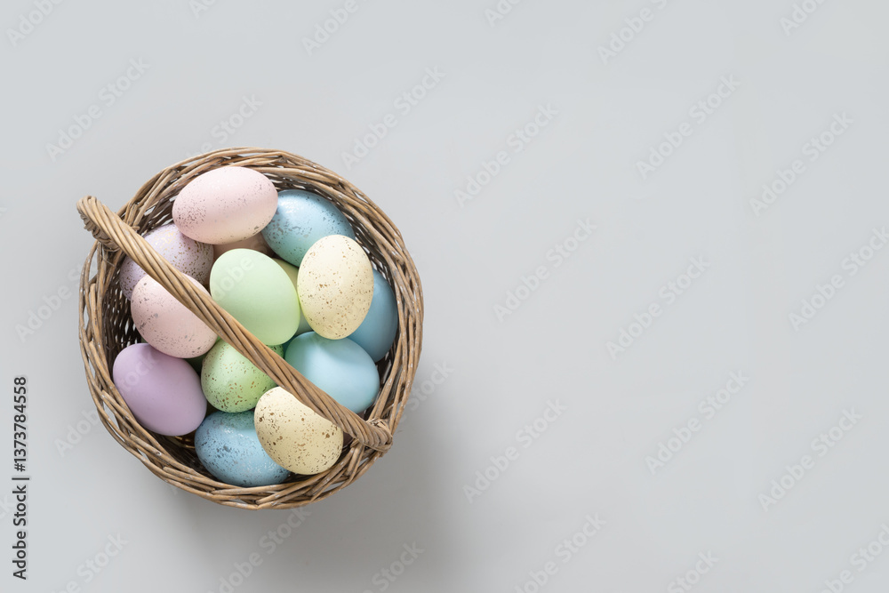 Easter pastel eggs in wicker basket for Happy holiday on gray background. View from above. Greeting card with copy space.