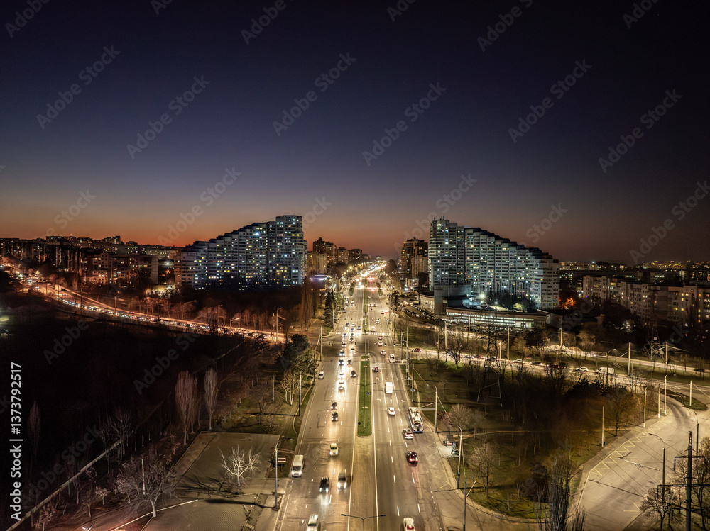 Drone view of the Chisinau Gates, the city symbol, above the busy Dacia Boulevard with cars at sunset and building lights in the evening