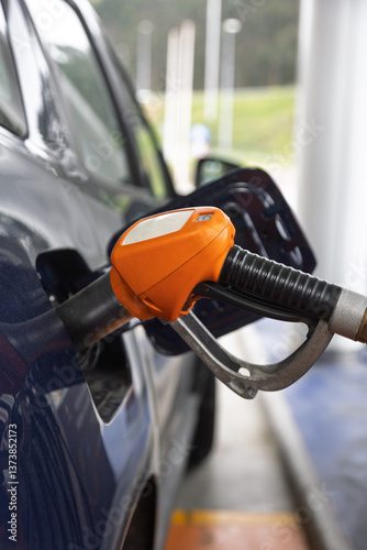 Orange fuel pump nozzle filling car at gas station