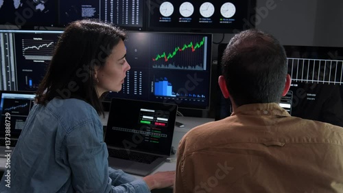 Stockbrokers discussing charts on multiple computer screens