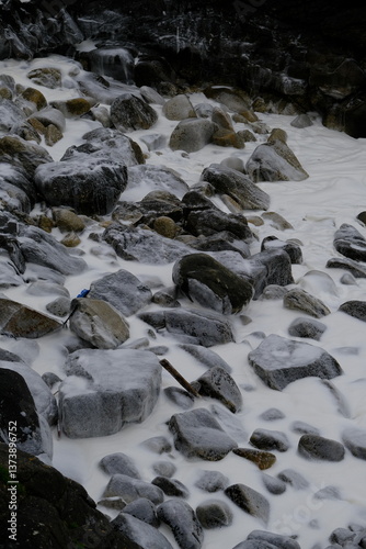 A close-up of some dark grey stones and with some white foam on the Atlantic shore. Batz-sur-Marne, France - April 6, 2024