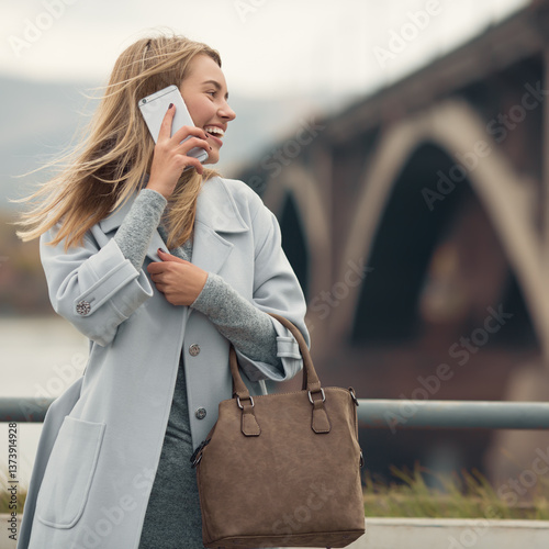 Young woman in blue coat talking phone. Autumn city background.