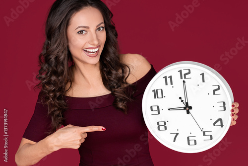 Happy young modern business woman in maroon dress point finger on clock