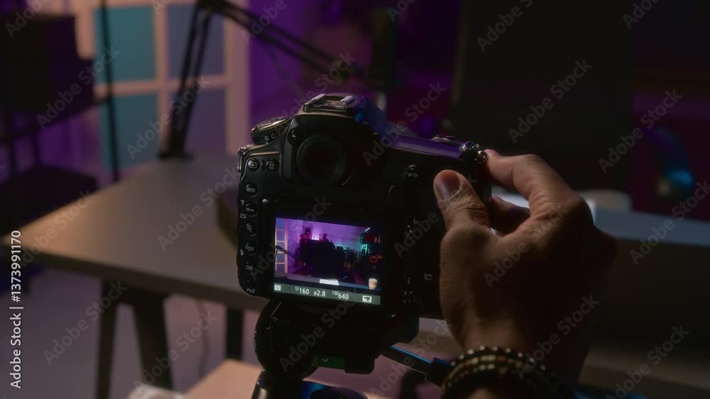 Closeup of hand of anonymous male streamer or content maker turning on camera on tripod, focusing on desk and adjusting light settings, while preparing for live stream on social media