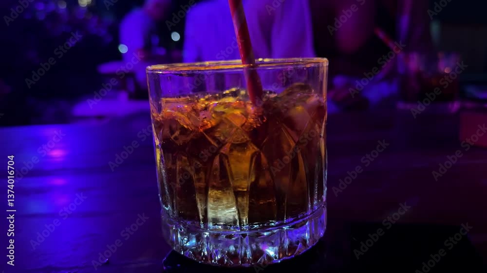 Hand is putting a glass of whisky back on the table after drinking. Ice is still rotating in glass. 