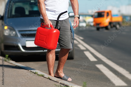 A man is standing by the roadside while holding a bright red gas can, looking for help