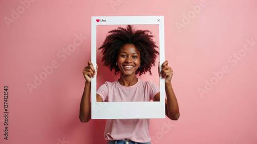 A smiling African woman playfully holds up a white picture frame towards the camera. Photo booth with likes. Social media frame.