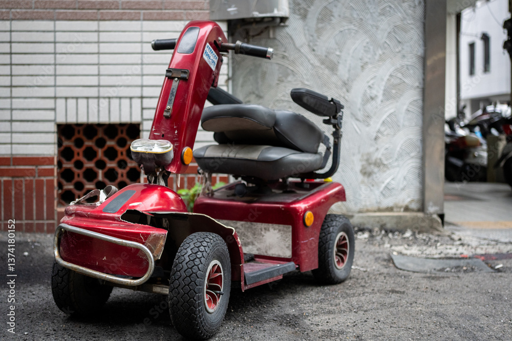 A damaged red mobility scooter sits on a city street, showing signs of wear and tear.